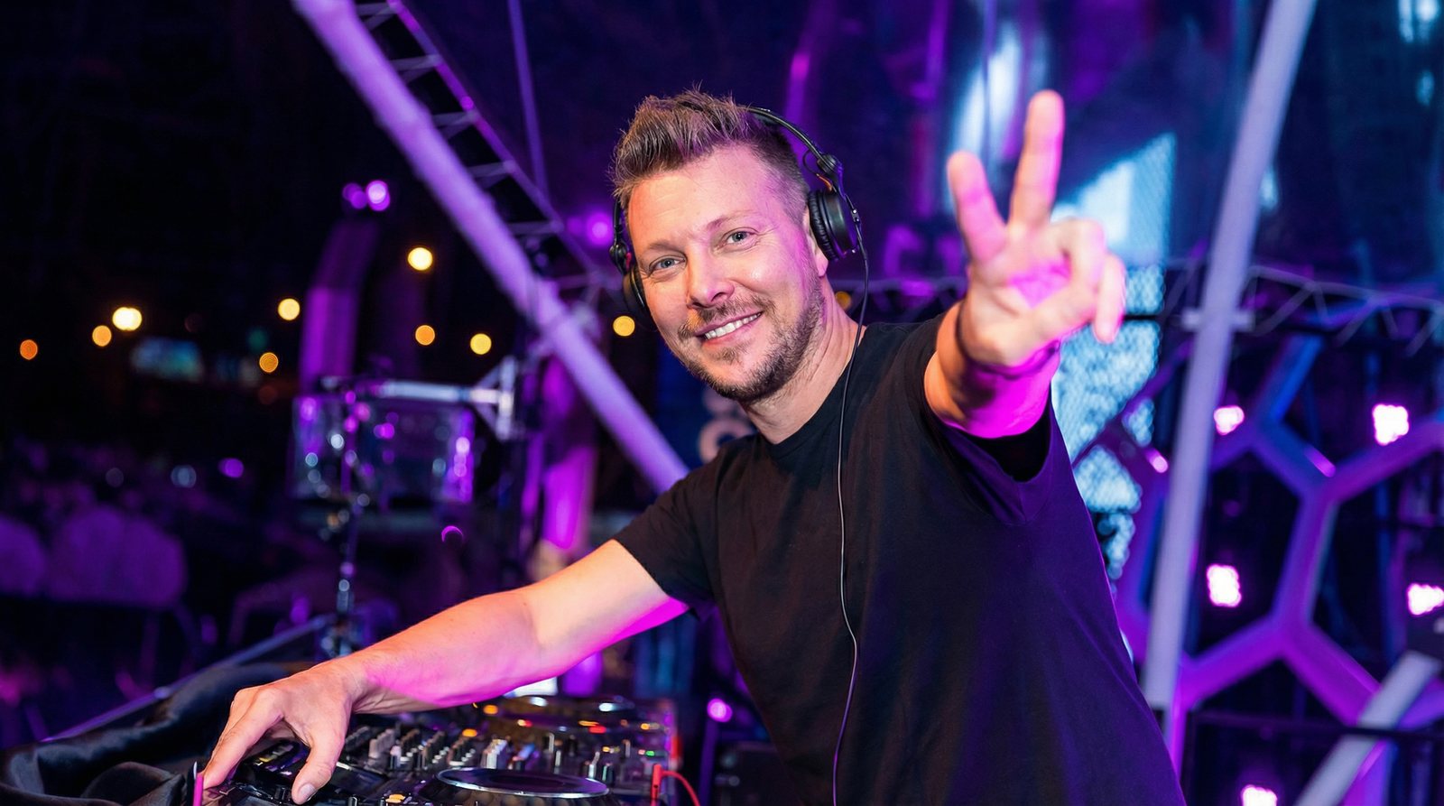 Robert bakom DJ-mixern på en festivalscen, leende med ett V-tecken mot publiken