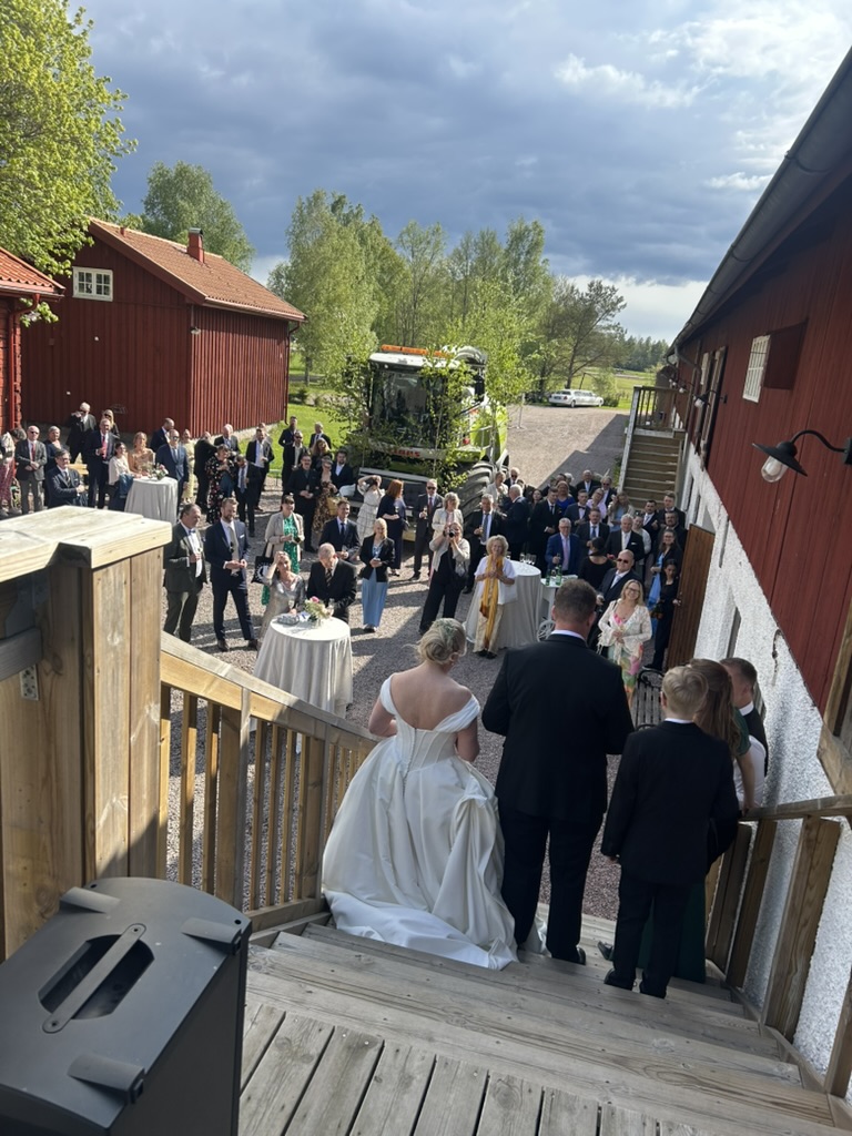 Brudpar går nerför trappan mot väntande gäster på en lantlig bröllopsgård